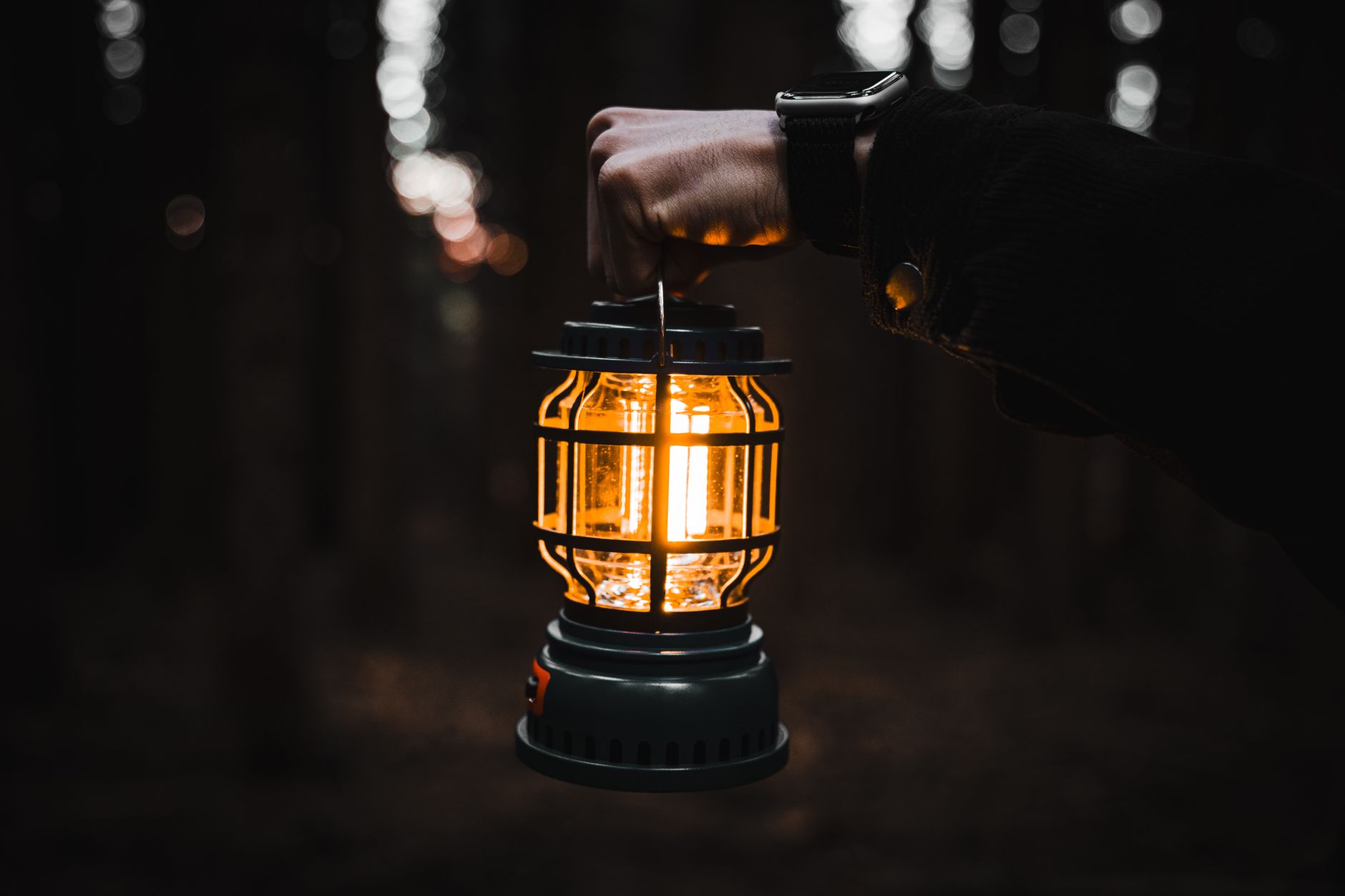 Person holding a glowing portable lantern in a dark room during a power outage