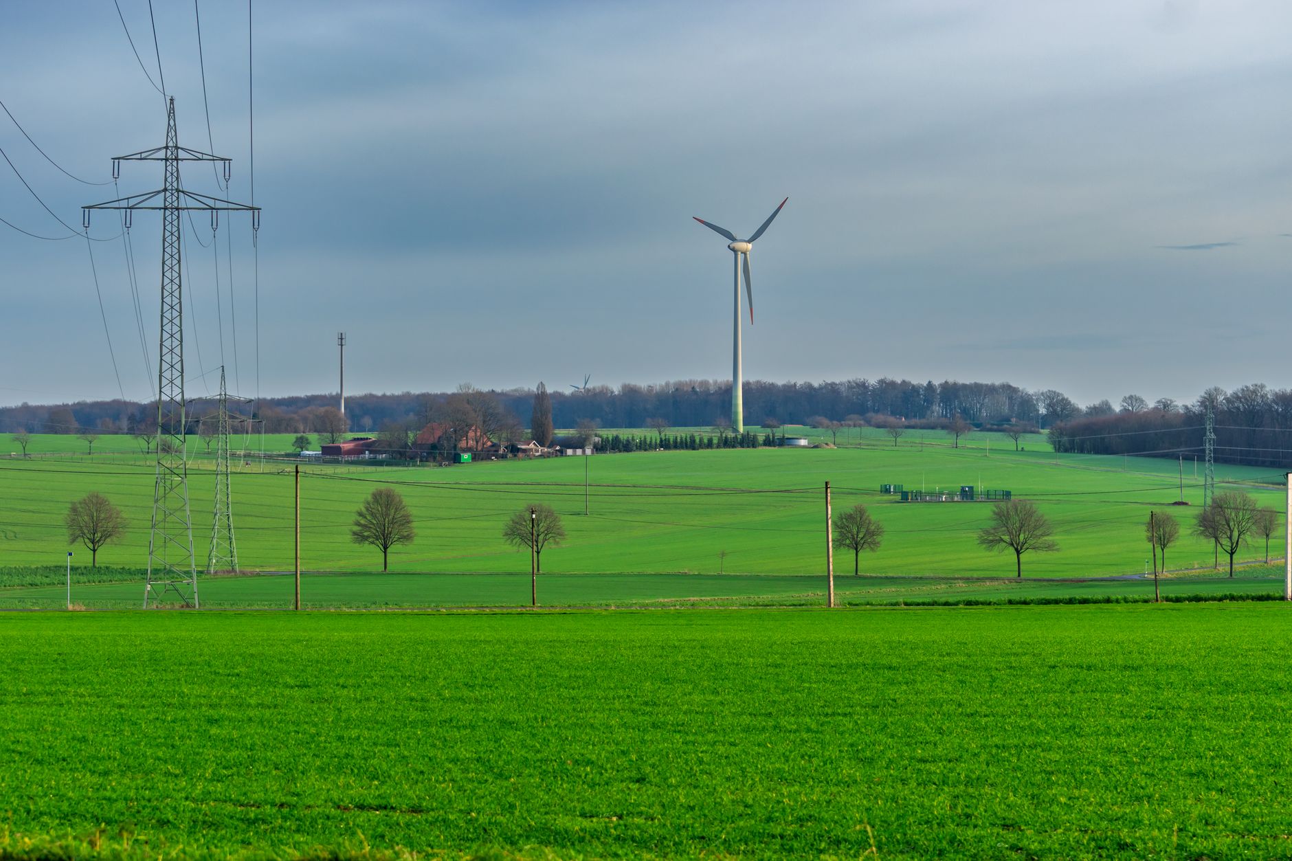 A small three-blade wind turbine mounted on a tall metal pole in a grassy field